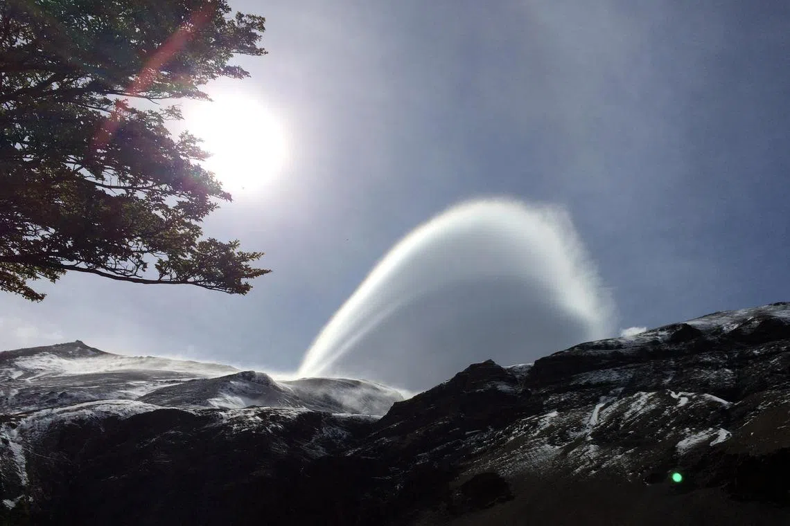 A rare cloud crafted by powerful winds into a curve in the sky, like a white rainbow in Patagonia. 
Patagonia is a sparsely populated region located at the southern end of South America, shared by Argentina and Chile.
