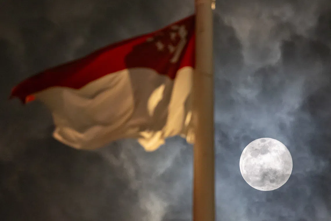 The Harvest Moon, the first of three supermoons in 2025, juxtaposed against the Singapore national flag, at Fullerton Hotel, on Oct 7, 2025. 