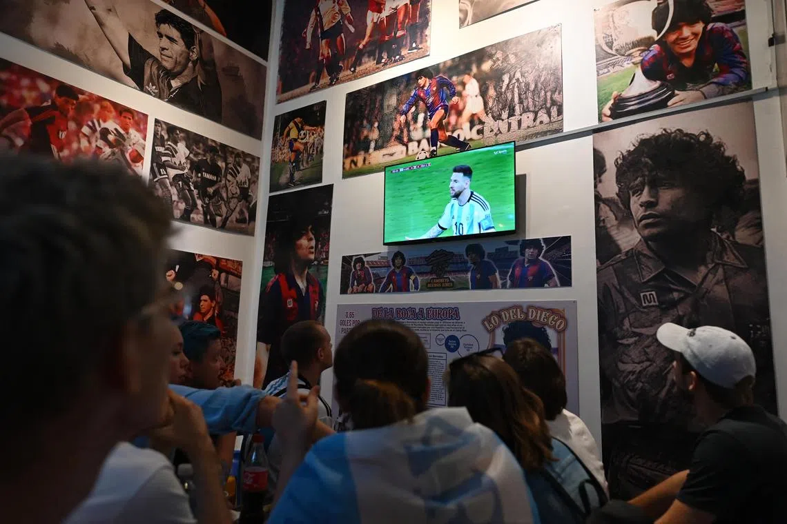 Argentina's Lionel Messi is seen on a screen surrounded by posters of former Argentina player Diego Maradona in Lo De Diego as fans watch the World Cup final against France. 