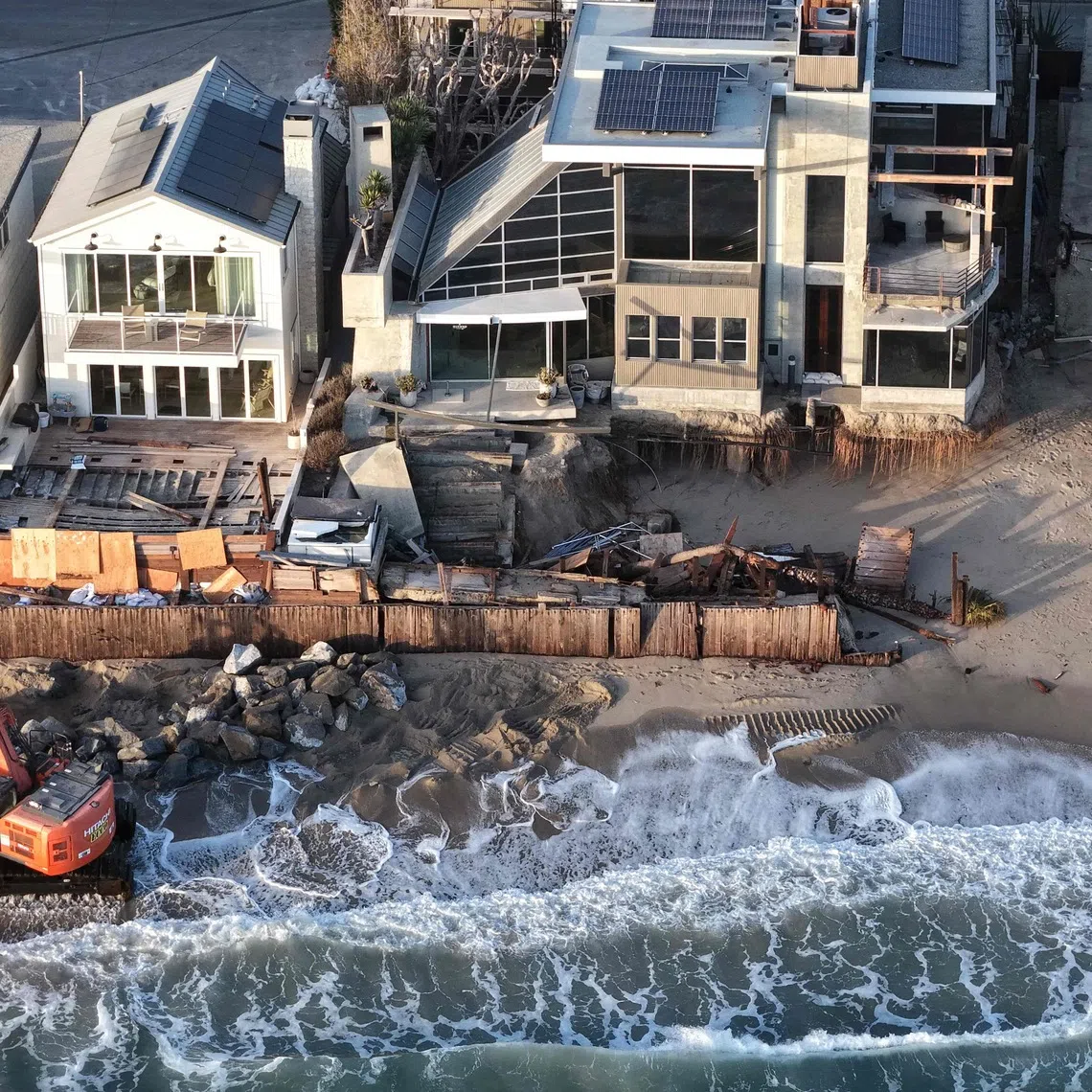 A Pacific Ocean wave washes up near a worker using heavy machinery to protect damaged beachfront homes with boulders on Sept 14, in Dana Point, California.