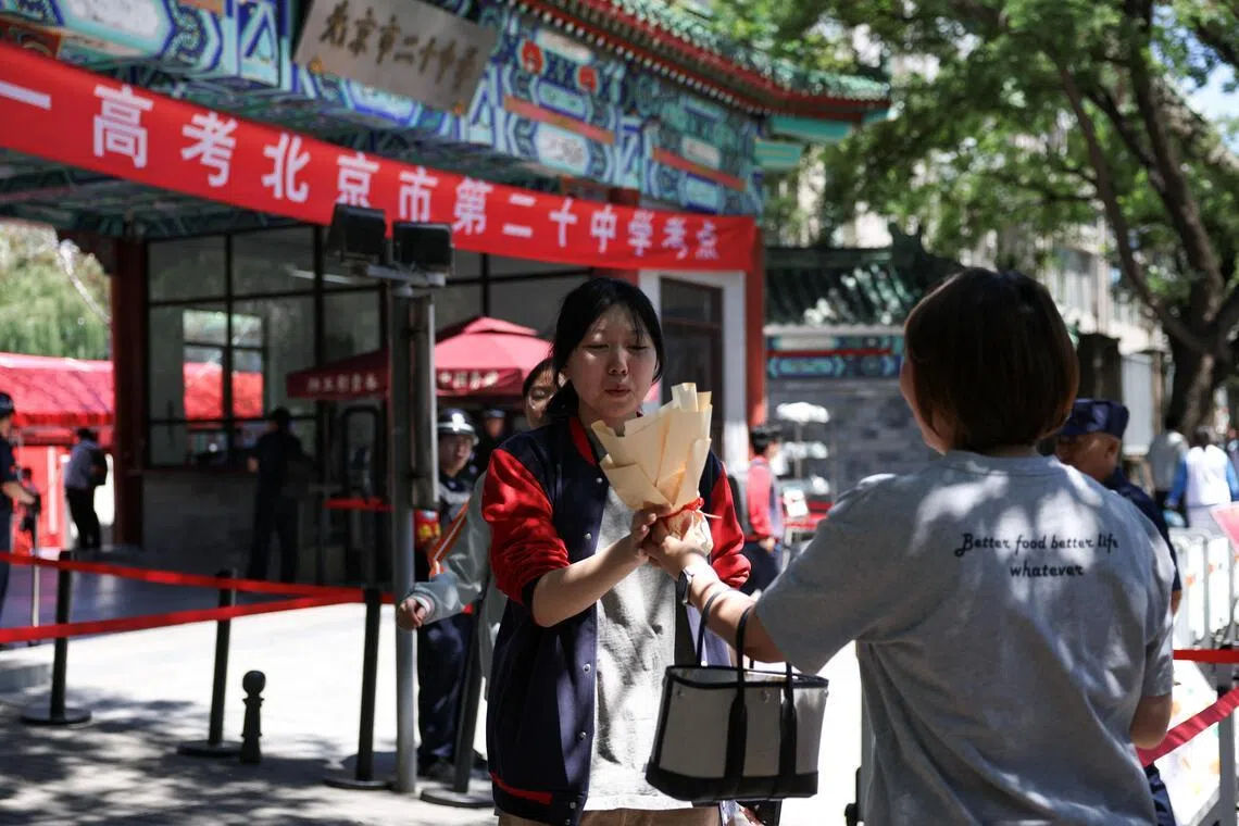 A mother passes flower to her daughter as students leave the venue after they finished the first exam in the annual “gaokao”, in Beijing on June 7.