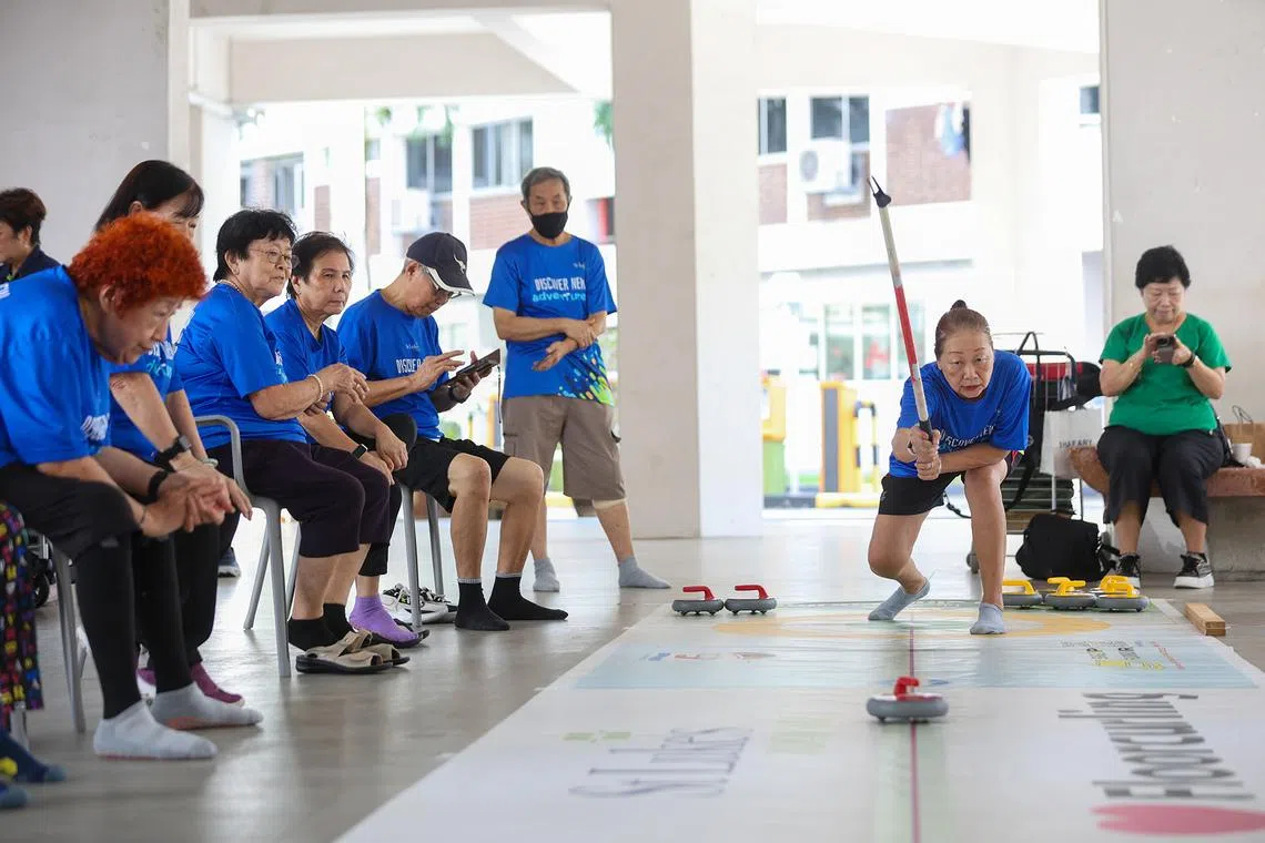 ST20260427_202651600842/Jasel Poh/jpcurling Retiree Agnes Chong follows through after releasing a rock during a game of floor curling at St Luke's ElderCare Active Ageing Centre (Care) @ Golden Years in Hougang on April 27, 2026. The 68-year-old has been playing the sport since May 2024 at the centre, where weekly sessions are held every Monday morning for two hours. The low impact variation of the winter sport helps keep seniors active mentally, requiring players to strategise the angle and strength of the release.