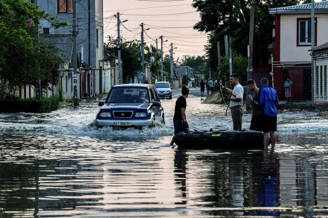 People stand next to an inflatable boat as a car drives past them on a flooded street in Kherson, Ukraine.