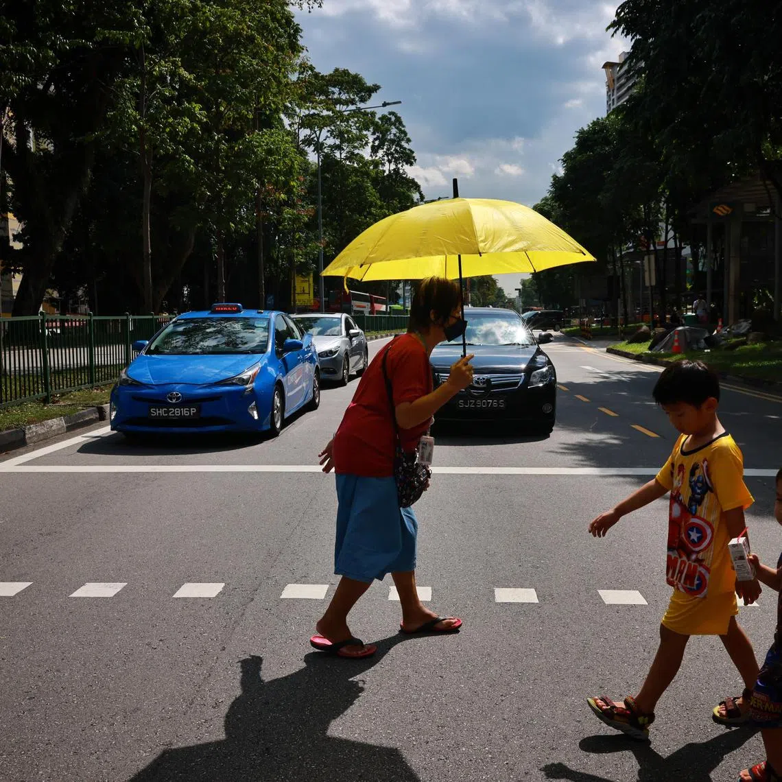 Elderly woman crossing the road using an umbrella to shade herself from the heat.