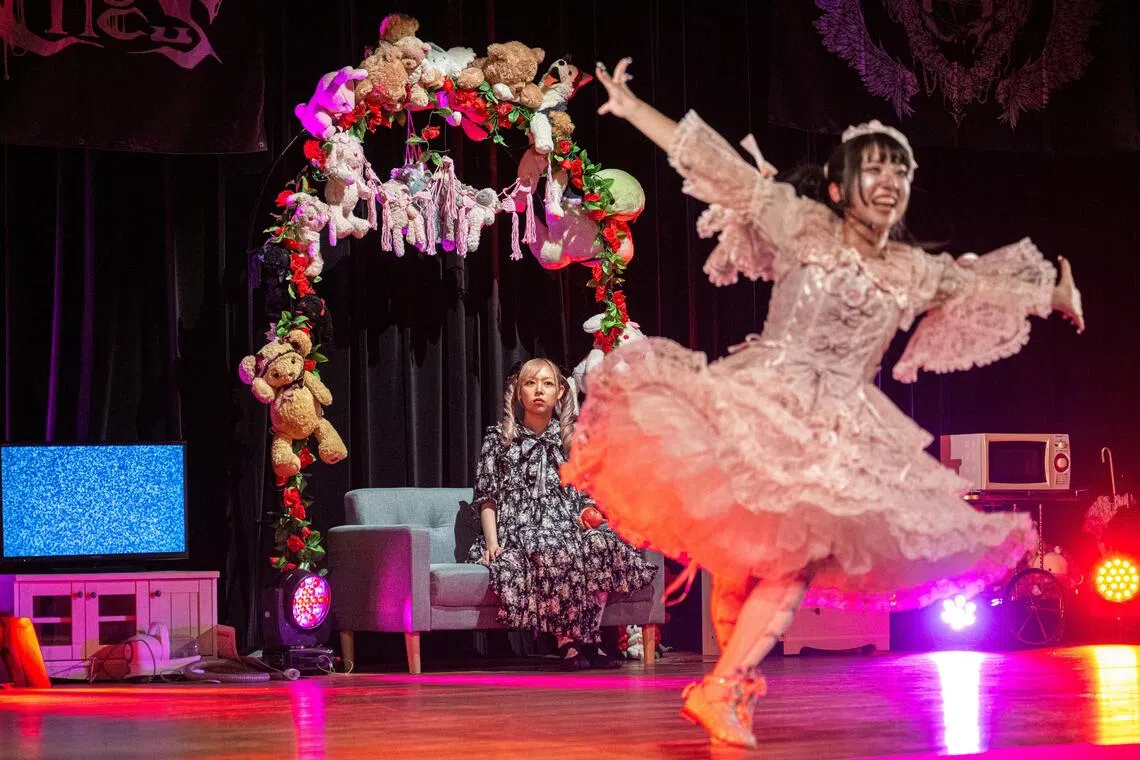 Donning frilly, doll-like dresses with voluminous skirts, young women on-stage whip out AI-generated photos of various men’s faces and ferociously rip them apart.