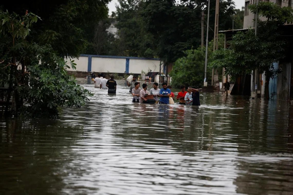 People carry their belongings to cross a flooded street after heavy rains in Ahmedabad, India, on Aug 28, 2024.