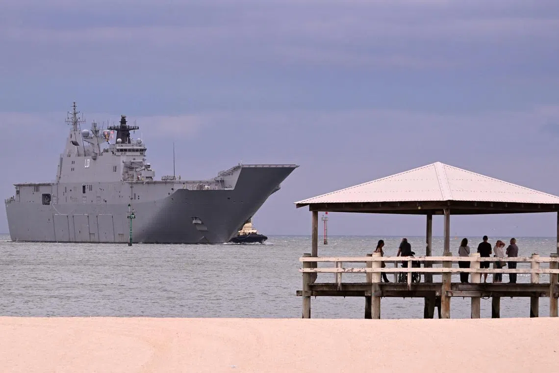 People look on as a tug escorts the HMAS Adelaide, a Royal Australian Navy (RAN) Canberra-class landing helicopter dock ship, while docking at Station Pier in Melbourne on March 19, 2024. (Photo by William WEST / AFP)