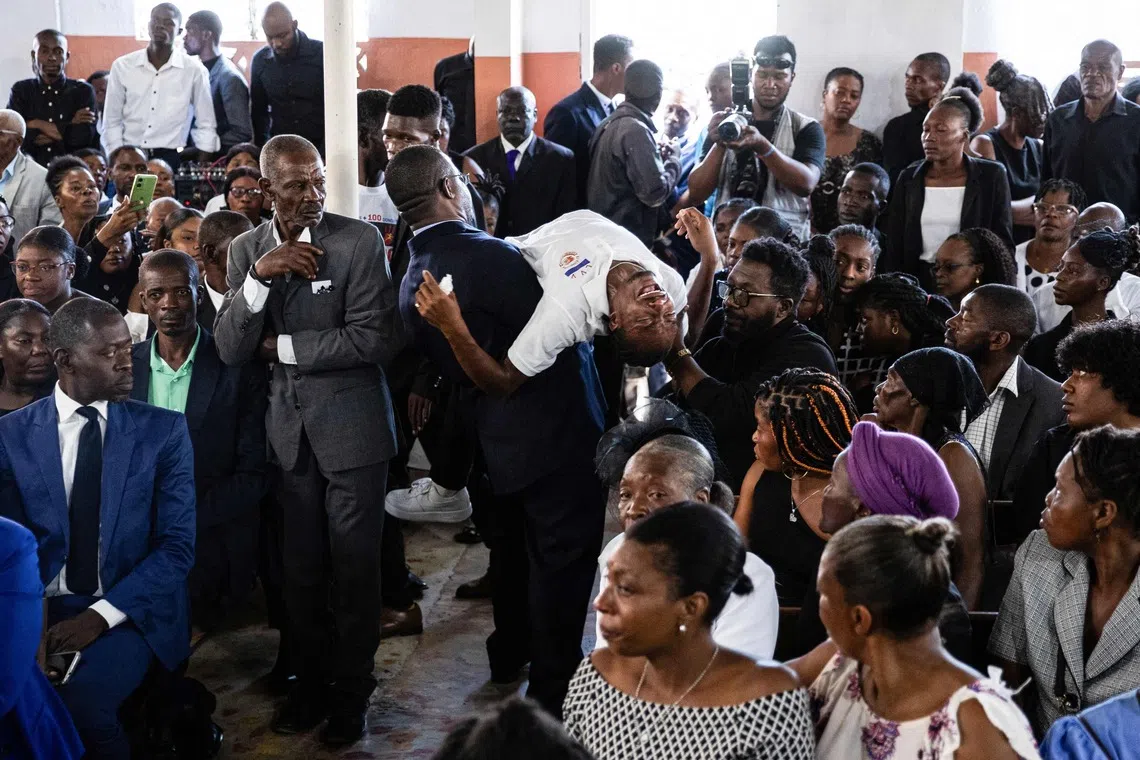 TOPSHOT - An overwhelmed man is carried out of a collective funeral service for more than twenty people killed by armed gangs last week in Kenscoff, a neighborhood near Port-au-Prince, on August 30, 2026. Gang members attacked displaced people huddling inside a church near Haiti's capital, killing around 40, some of them execution-style, the mayor told AFP on August 24. (Photo by Clarens SIFFROY / AFP)