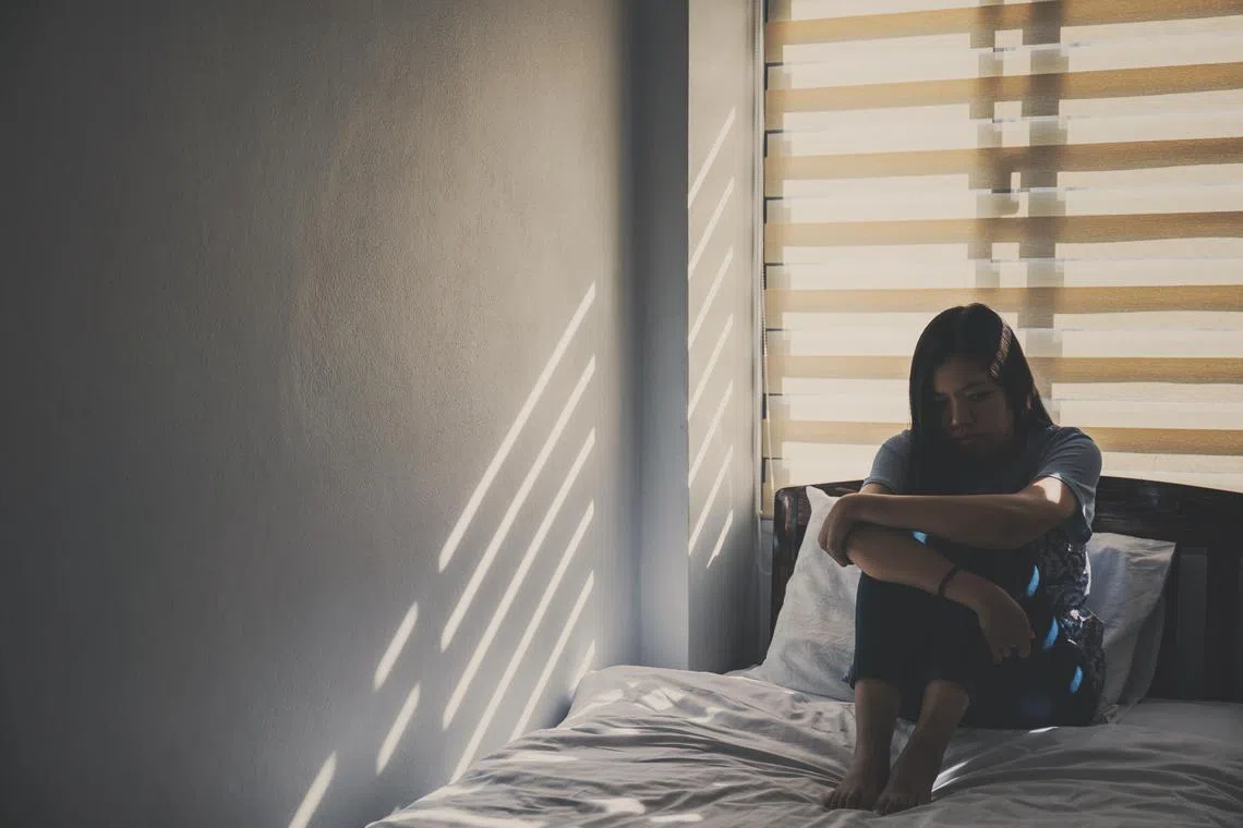 Asian women are sitting hugging their knees in bed. Feeling sad, disappointed in love In the dark bedroom and sunlight from the window through the blinds.Vintage tone.
