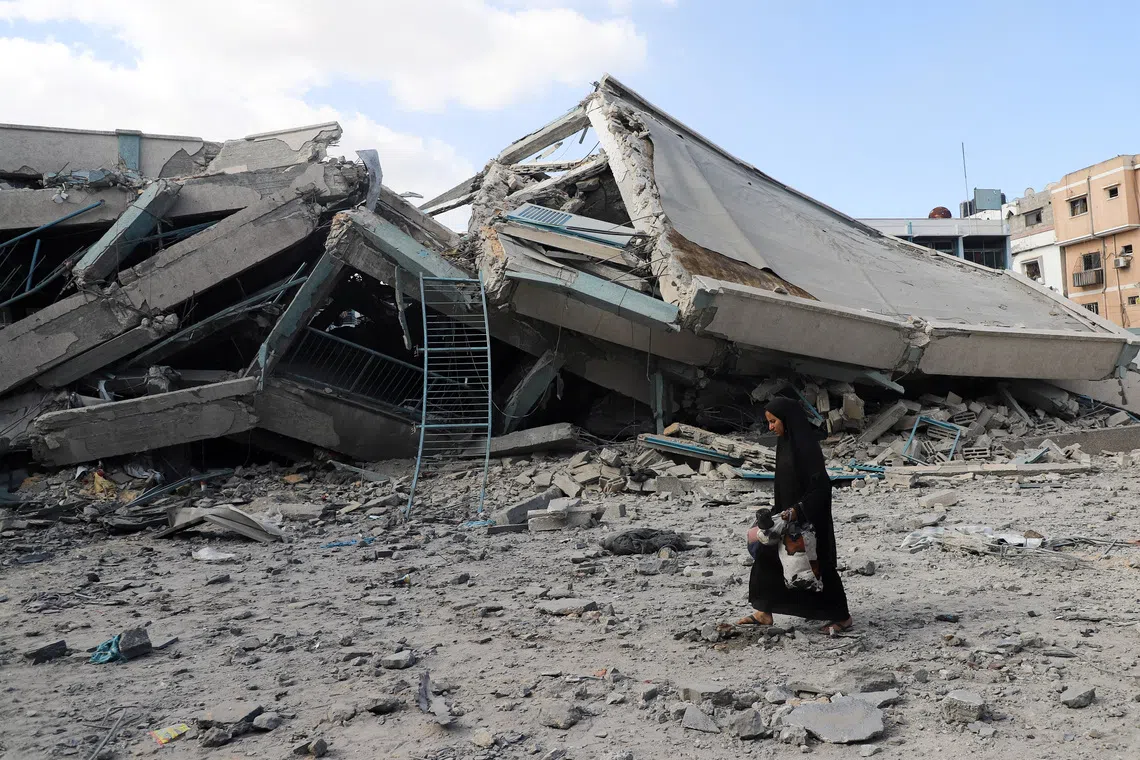 A Palestinian woman carries belongings as she walks amid debris at a United Nations school where displaced people were taking shelter, after it was hit in overnight Israeli strikes, amid an Israeli military operation, at Zeitoun neighbourhood in Gaza City, October 1, 2025. REUTERS/Ebrahim Hajjaj