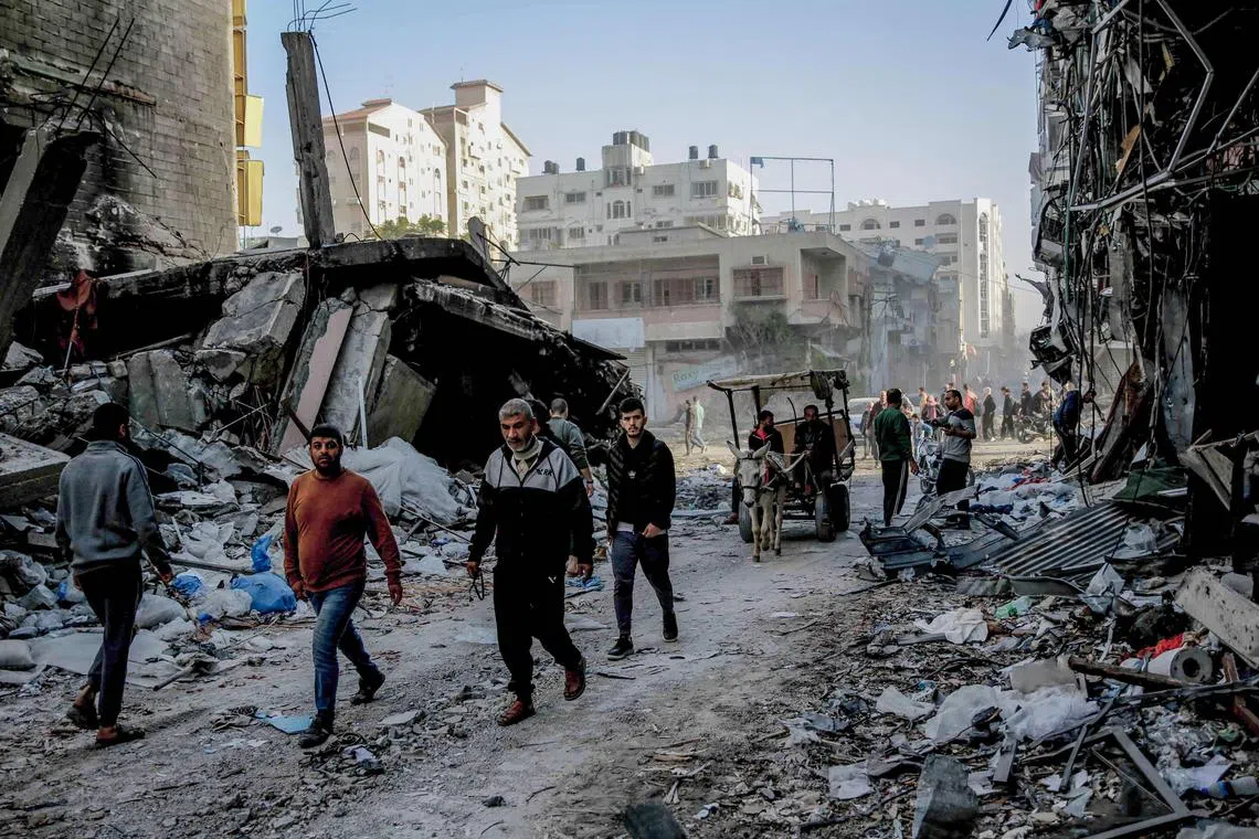 Palestinians walk amid the rubble of destroyed buildings in Gaza City, as a four-day ceasefire between Hamas and Israel takes effect