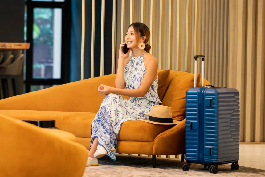 Best luggage brands in Singapore: Woman sitting on couch taking a call, with luggage bag beside her