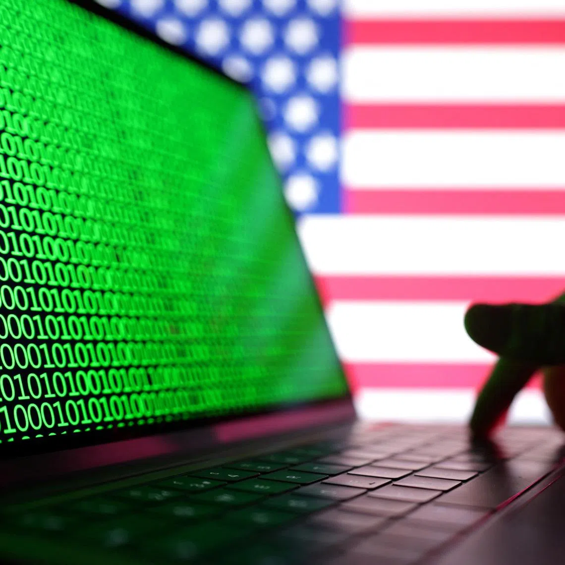 A hand is seen on a laptop with binary codes displayed in front of the USA flag in this illustration taken, August 19, 2022. REUTERS/Dado Ruvic/Illustration