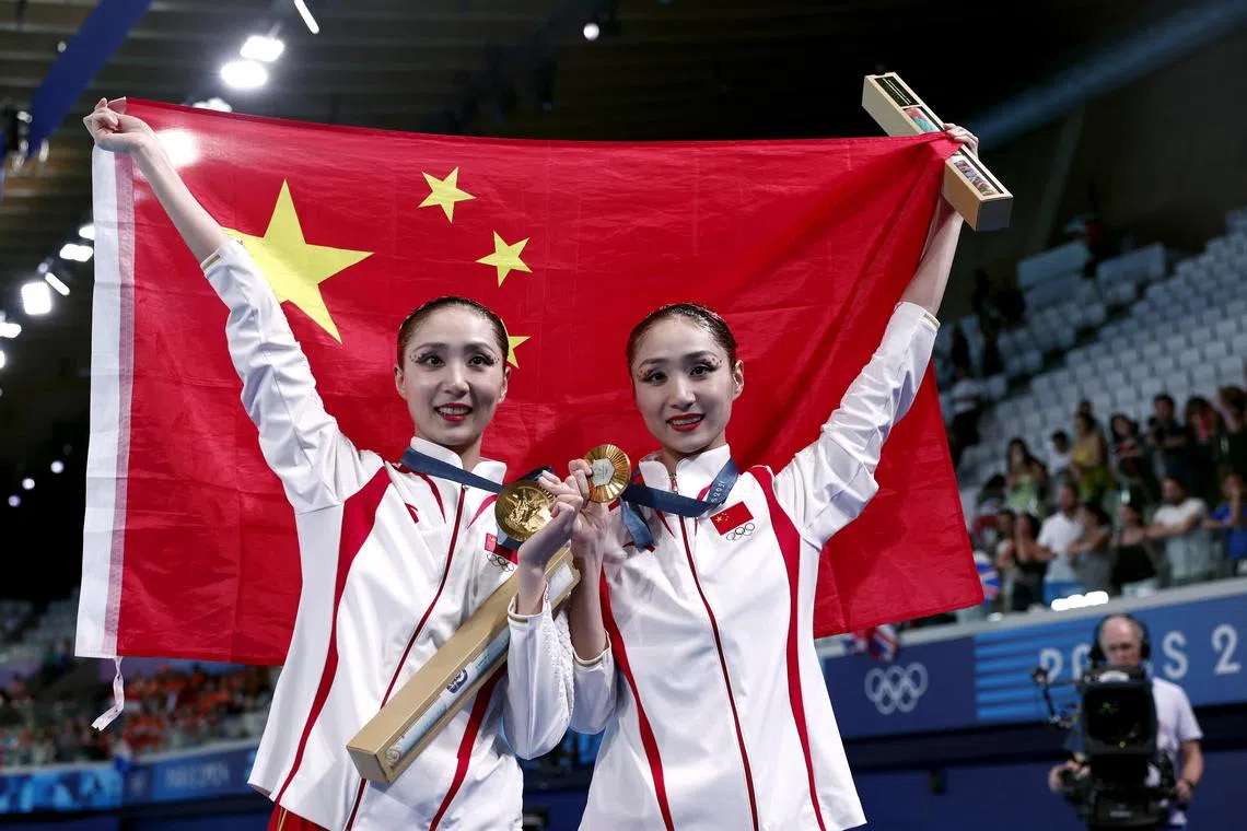 Gold medallists in artistic swimming Wang Liuyi and Wang Qianyi pose for pictures with their medals and the flag of China. 
