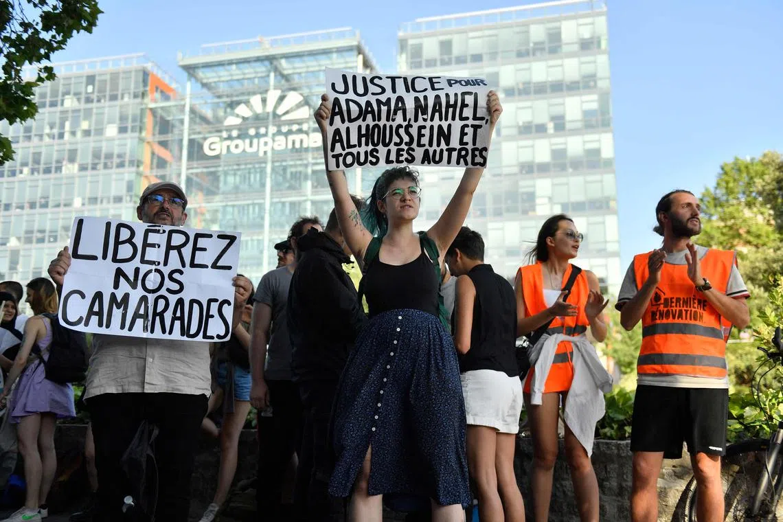 People hold placards reading "Justice for Adama, Nahel, Alhoussein and all the others" (R) and "Free our comrades", in a Paris protest against "state racism".