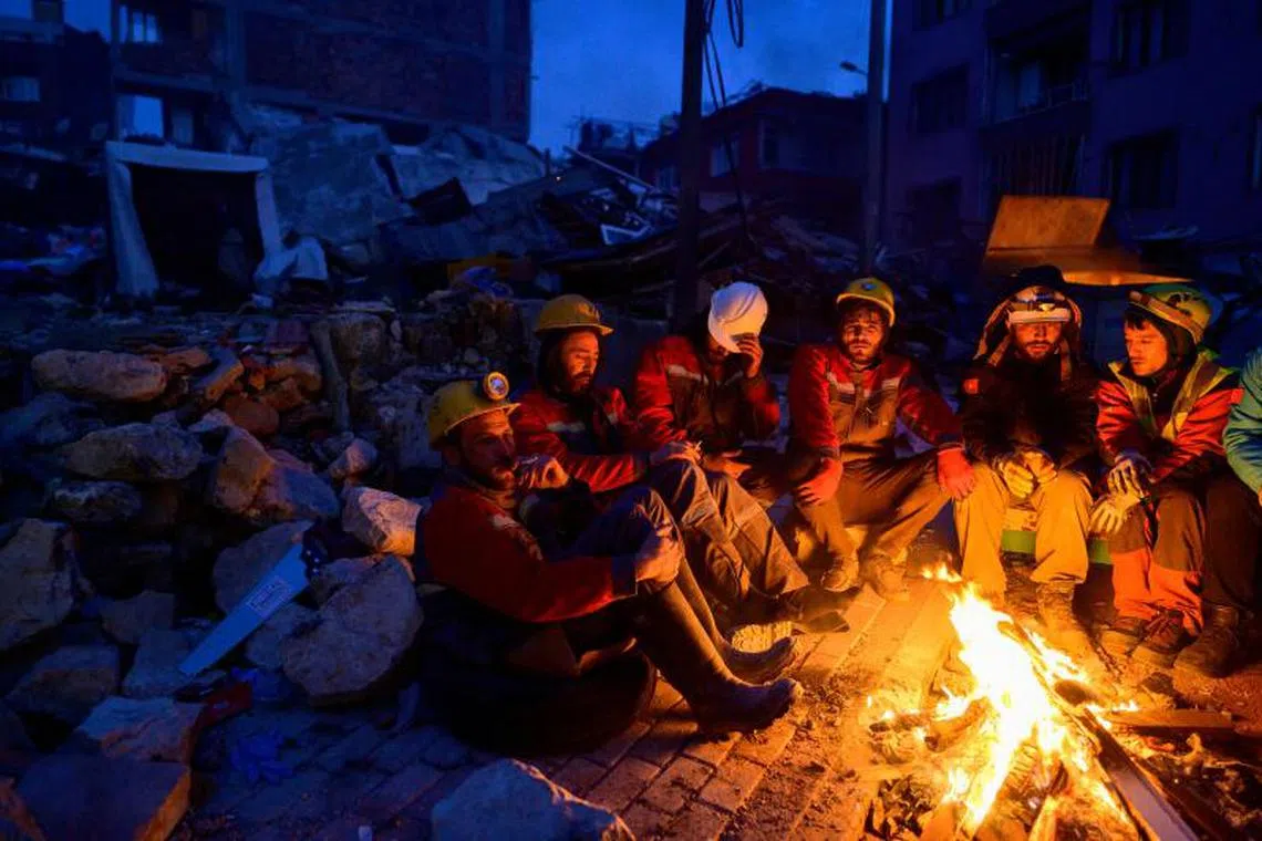 Rescuers sit by a bonfire in Hatay, on February 12, 2023, after a 7.8-magnitude earthquake struck the country's south-east. The death toll from a massive earthquake that hit Turkey and Syria climbed to more than 20,000, as hopes faded of finding survivors stuck under rubble in freezing weather. PHOTO : AFP