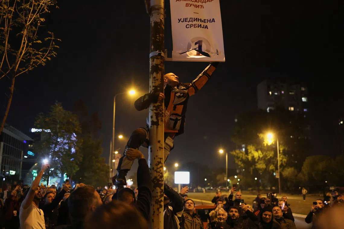 Image 7: A supporter of the electoral list "Student List - Students Win" damages a banner of Serbia's former President and the ruling Serbian Progressive Party (SNS) prime ministerial candidate Aleksandar Vucic as others celebrate following the first results of the parliamentary election in Belgrade, Serbia, October 25, 2026. REUTERS/Marko Djurica