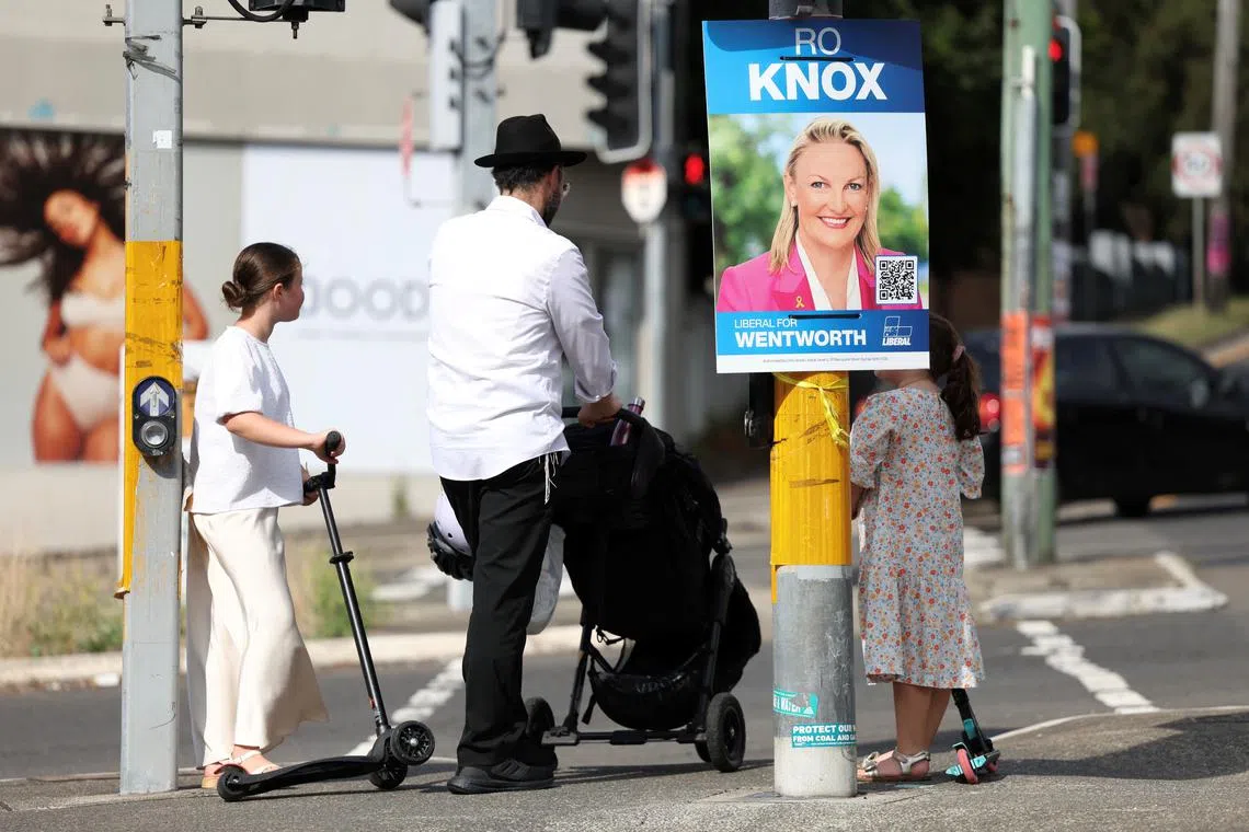 A man waits with his children at a traffic light next to a campaign sign depicting Wentworth candidate Ro Knox, of the Liberal party, in North Bondi, Australia, March 22, 2025. REUTERS/Hollie Adams