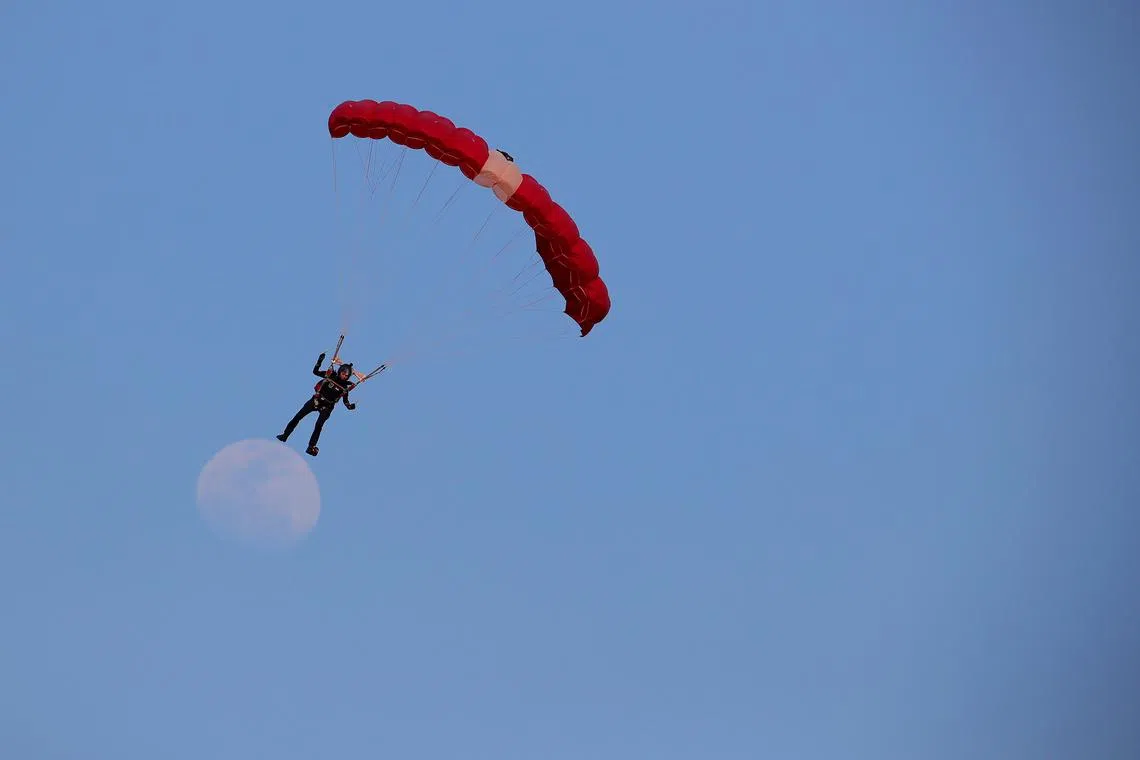 Parachutist 2WO Shirley Ng, one of the team of 10 Red Lions, descending at the Marina Bay floating platform around 6pm at the National Day Parade 2022 with a faint image of the moon in the background, 9 August 2022. The Red Lions will only jump over the Padang at NDP 2023.