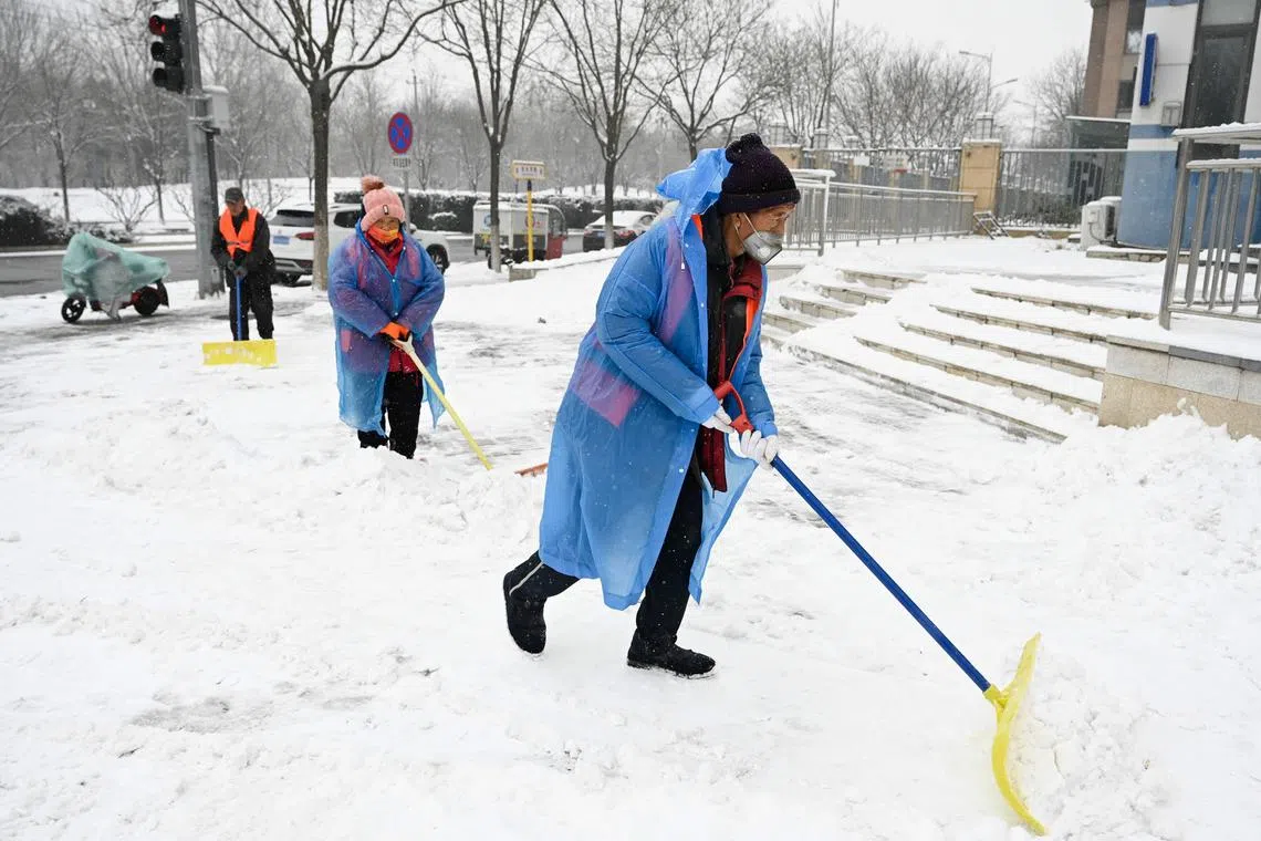 People clear snow from a sidewalk on a snowy day in Beijing on Dec  13.