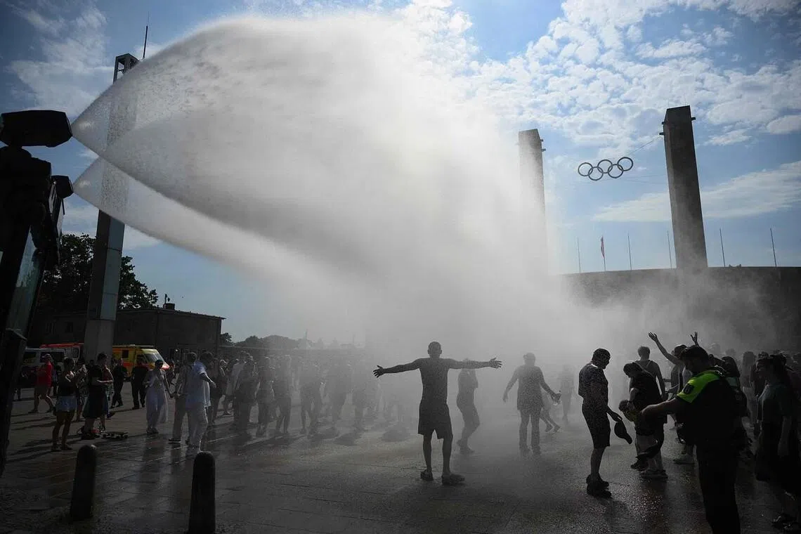 TOPSHOT - Police use water cannon to spray people with water as the arrive at the Olympic stadium for a concert of US singer Bruno Mars on June 28, 2026, in Berlin, as the German capital is expected to reach temperatures around 40 degrees Celsius during a heatwave in Europe. Tens of millions are braving a weekend of extreme temperatures in Europe as a deadly heatwave moves eastwards, with some countries announcing rising death tolls and health services warning of saturation. While some mild relief is expected Sunday in western Europe, German forecasters are warning that more temperature records could still be broken over the weekend as eastern countries issue a slew of red alerts for the coming days. (Photo by RALF HIRSCHBERGER / AFP)