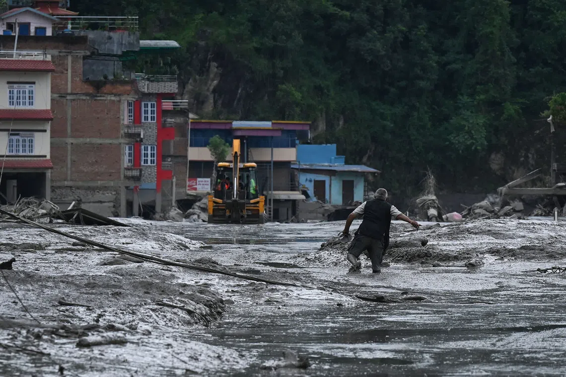 A resident walks along a street covered in mud following flash floods and a landslide disaster in Devghat, in Nepal's Nuwakot district on August 26, 2026. A massive flood and landslide disaster on the Nepal-Tibet border killed at least 103 people on August 26, 2026 and left several hundred missing, many of them foreign tourists. Aid workers said entire settlements had been "wiped out". Some 403 tourists -- 341 of them foreigners -- were unaccounted for several hours after the disaster struck, according to the tourism ministry. (Photo by PRAKASH MATHEMA / AFP)