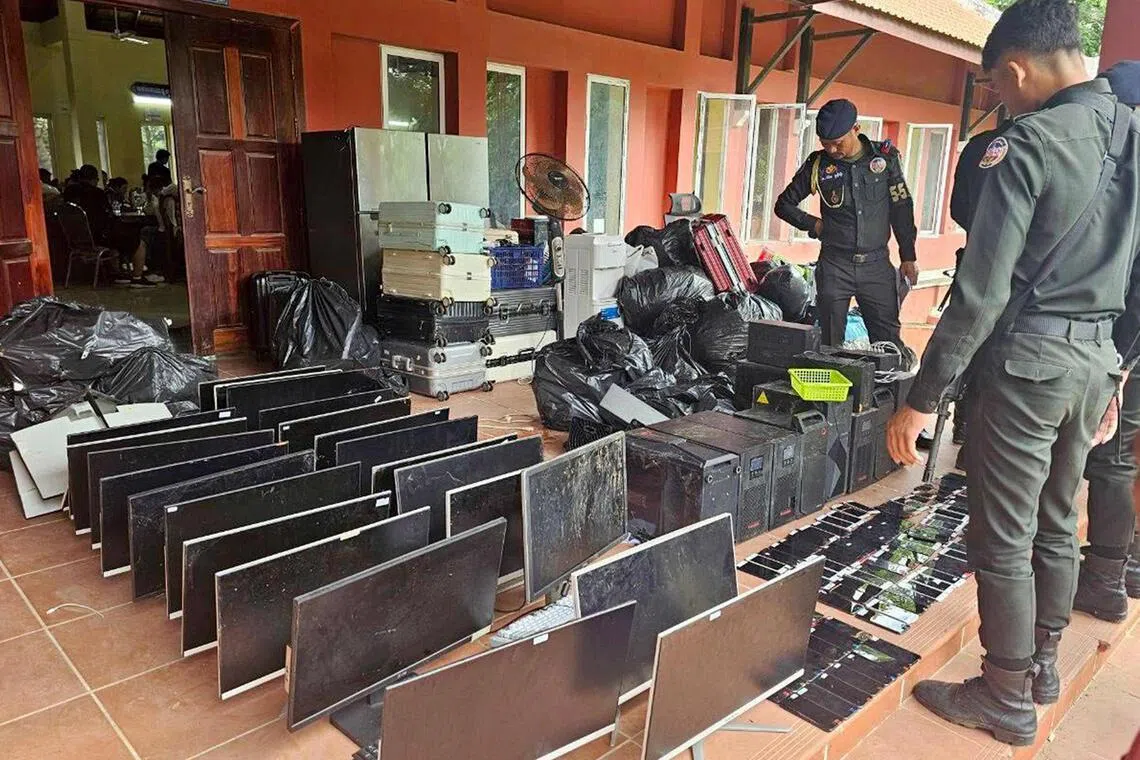 This pool photo taken on July 17, 2025 and released on July 18 by Agence Kampuchea Presse (AKP) shows military police looking at computers, smartphones and other equipment seized during a raid on a scam centre in Kandal province. The number of suspects arrested in a Cambodian crackdown on internet scam centres has risen to 2,000, a government minister told AFP on July 18. (Photo by POOL / AFP)