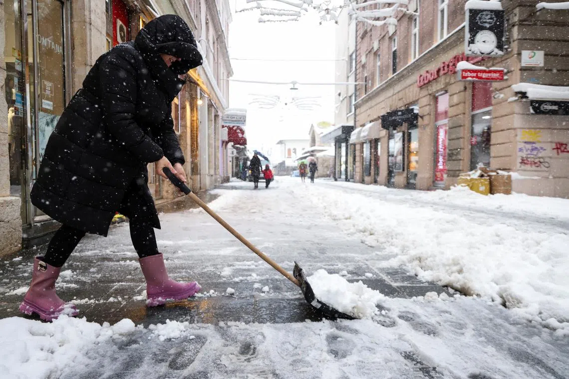 A woman shovels snow on the main street during snowstorm in Sarajevo, Bosnia and Herzegovina, December 24, 2024.REUTERS/Amel Emric