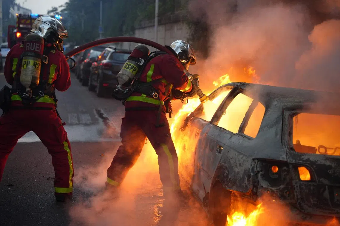 Firefighter extinguish a burning vehicle destroyed by protesters in Nanterre, west of Paris, late on June 27, 2023, after French police killed a teenager who refused to stop for a traffic check in the city. 