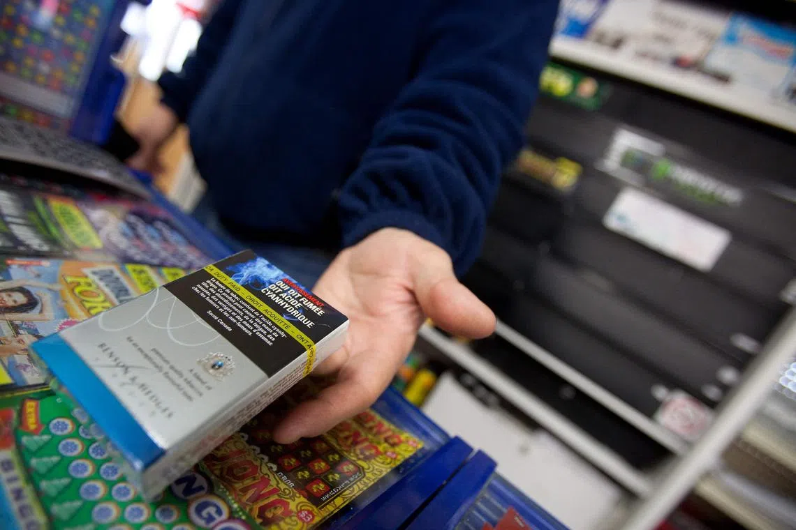 (FILES) A corner store owner in St. Thomas, Ontario, Canada, holds a package of cigarettes on March 12, 2012. Canada will soon require that health warnings be printed on individual cigarettes and cigars in a further crackdown on smoking, Canadian Addictions Minister Carolyn Bennett announced May 31, 2023. The messaging, to be phased in starting August 1, will include lines such as "Poison in every puff," "Tobacco smoke harms children" and "Cigarettes cause cancer." (Photo by GEOFF ROBINS / AFP)
