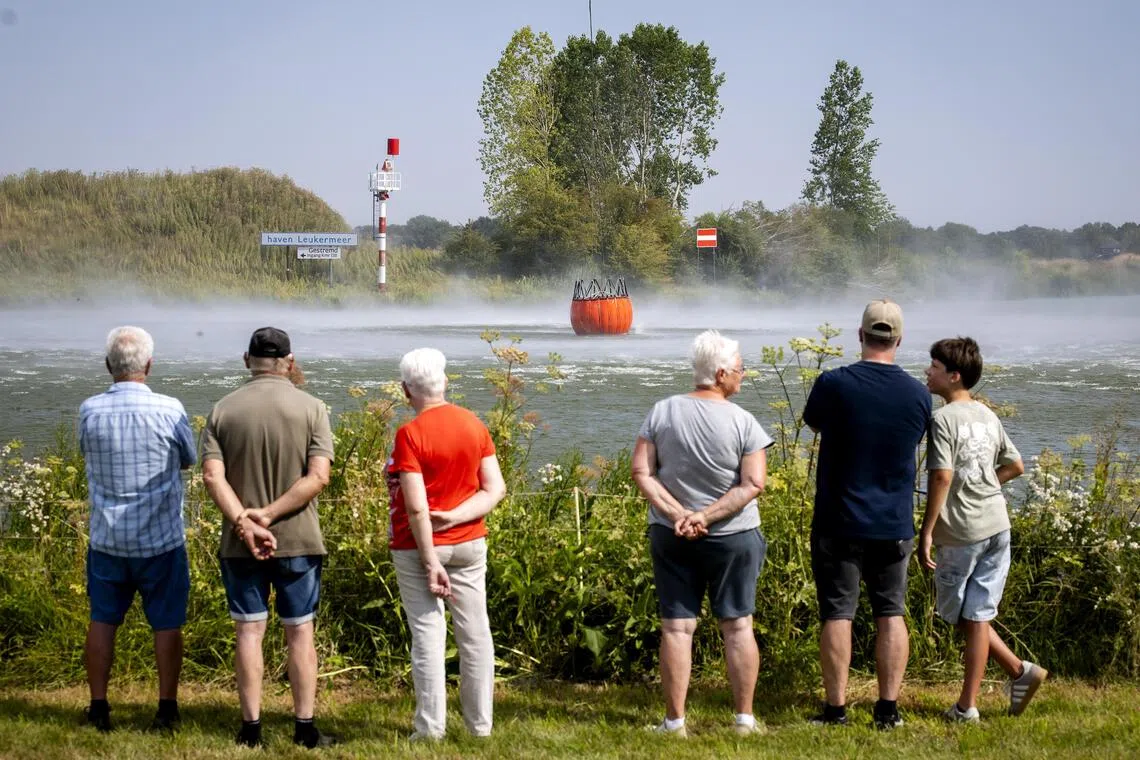 Day-trippers watch as a water bucket suspended beneath a Chinook helicopter is filled from the Meuse River in the Netherlands, on Aug 4, during operations to combat a wildfire in the Boschhuizerbergen nature reserve.