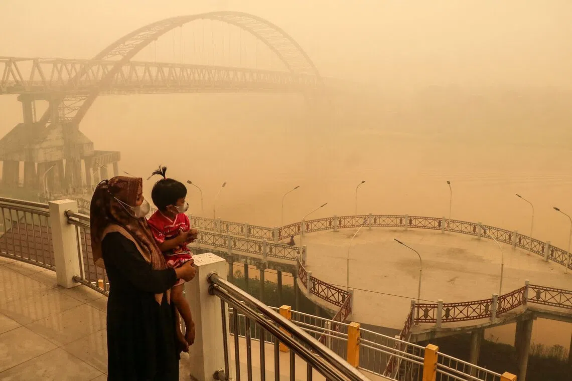 TOPSHOT - A child and mother wearing face masks look on from a bridge amid thick haze from forest and land fires in the region in Palangkaraya, Central Kalimantan, on October 12, 2026. Toxic haze has shrouded parts of Indonesia, Malaysia and Singapore for weeks as Jakarta struggles to contain fires that have scorched large tracts of Borneo and Sumatra, with the smoke drifting across the region. (Photo by REINA / AFP)