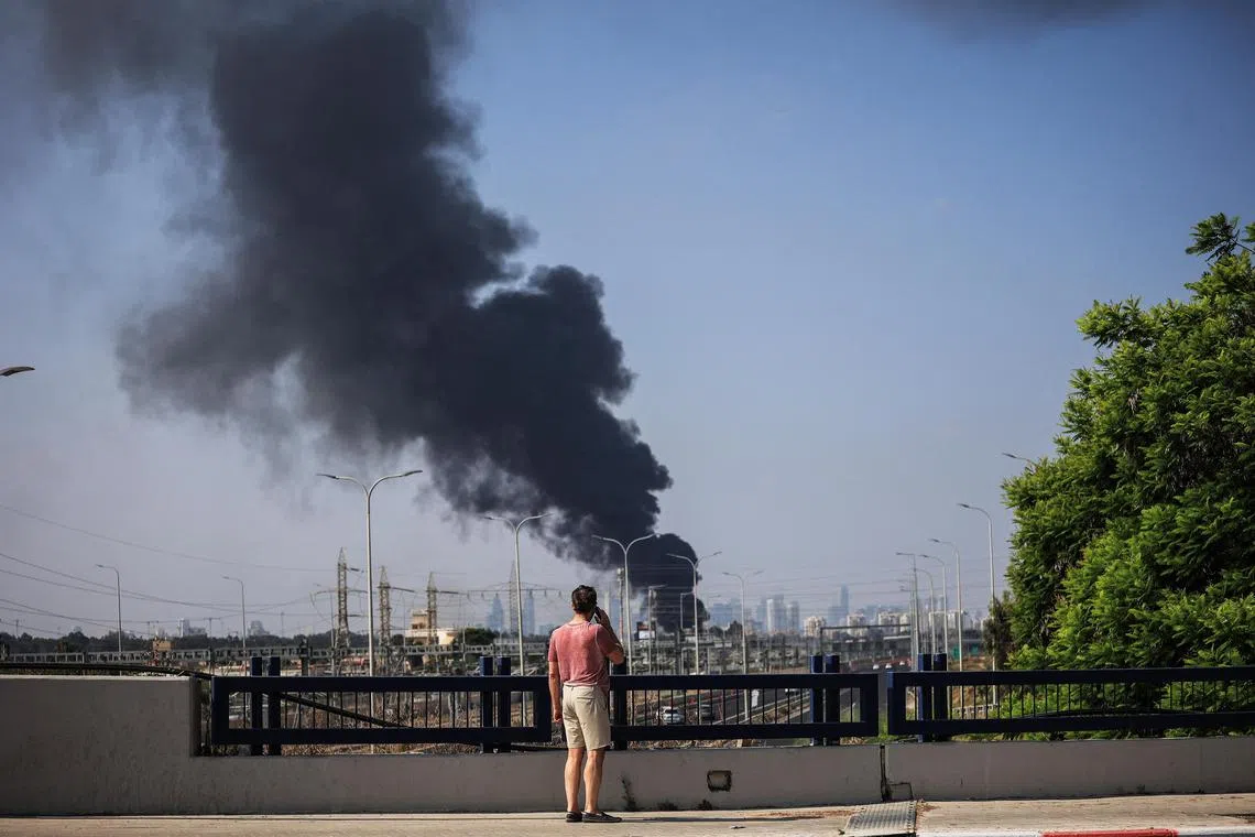 An Israeli man looks at smoke that rises following a missile attack from Iran, in Herzliya, Israel, on June 17, 2025.
