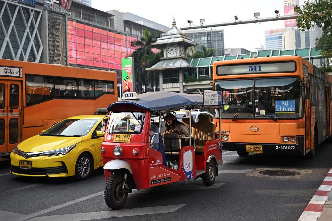 A commuter rides in an electric tuk tuk on the streets of Bangkok.