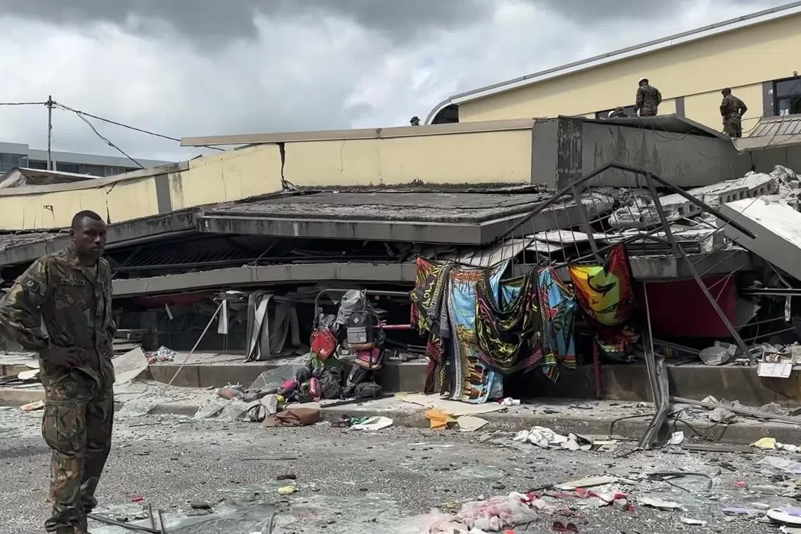 A soldier standing beside a collapsed building following an earthquake in Port Vila, Vanuatu.