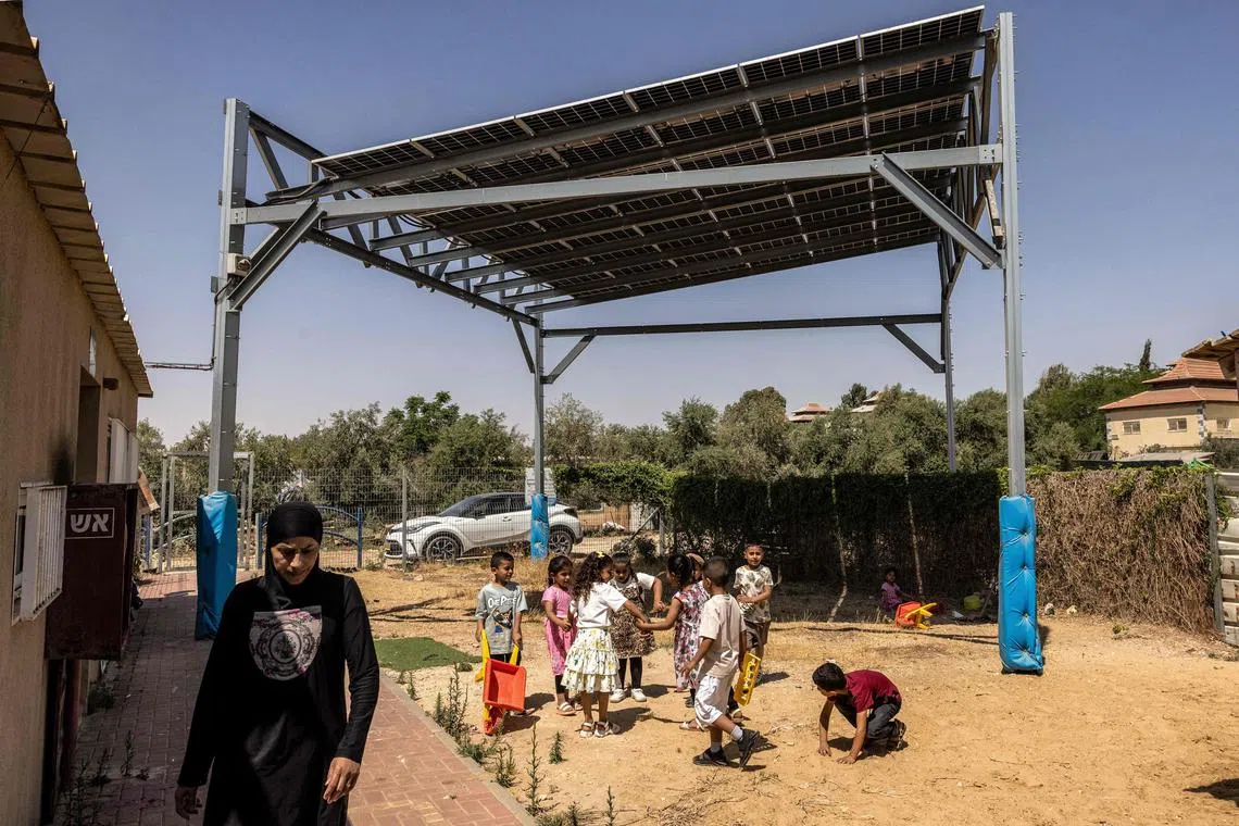Children play beneath a scaffolding holding photovoltaic solar panels in the yard of a kindergarten in the recognised but unplanned Bedouin village of Umm Batin near Beersheva in Israel's southern Negev Desert on June 11, 2025. 