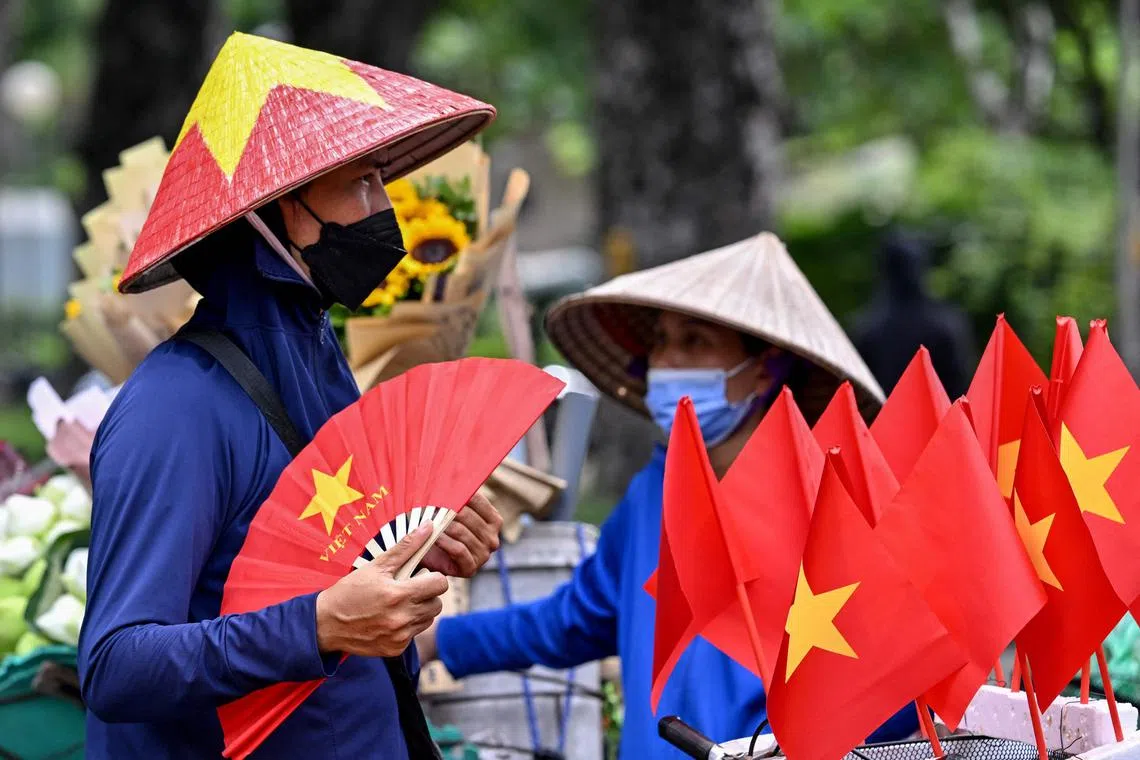 A street vendor uses a hand fan to beat the heat next to small Vietnamese national flags for sale in Hanoi on August 5, 2025. Northern Vietnam was sweltering under a blistering heatwave August 5 with 17 districts setting record highs for the month, as power cuts were predicted due to the electricity grid struggling with demand. (Photo by Nhac NGUYEN / AFP)