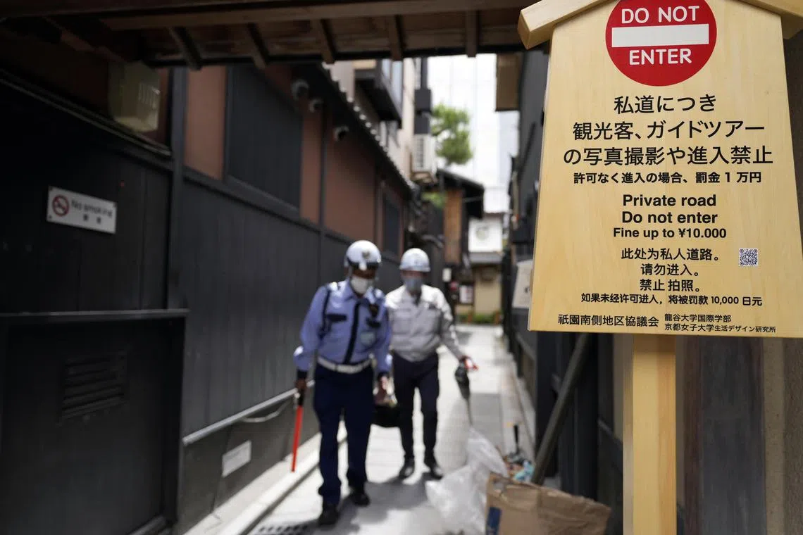 Workers walk past a board they just installed to stop tourists from entering a private alley in Gion district, Kyoto, western Japan, on May 29, 2024.