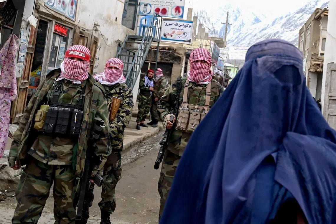 Taliban security personnel stand guard as an Afghan burqa-clad woman (right) walks along a street at a market in the Baharak district of Badakhshan province on Feb 26.