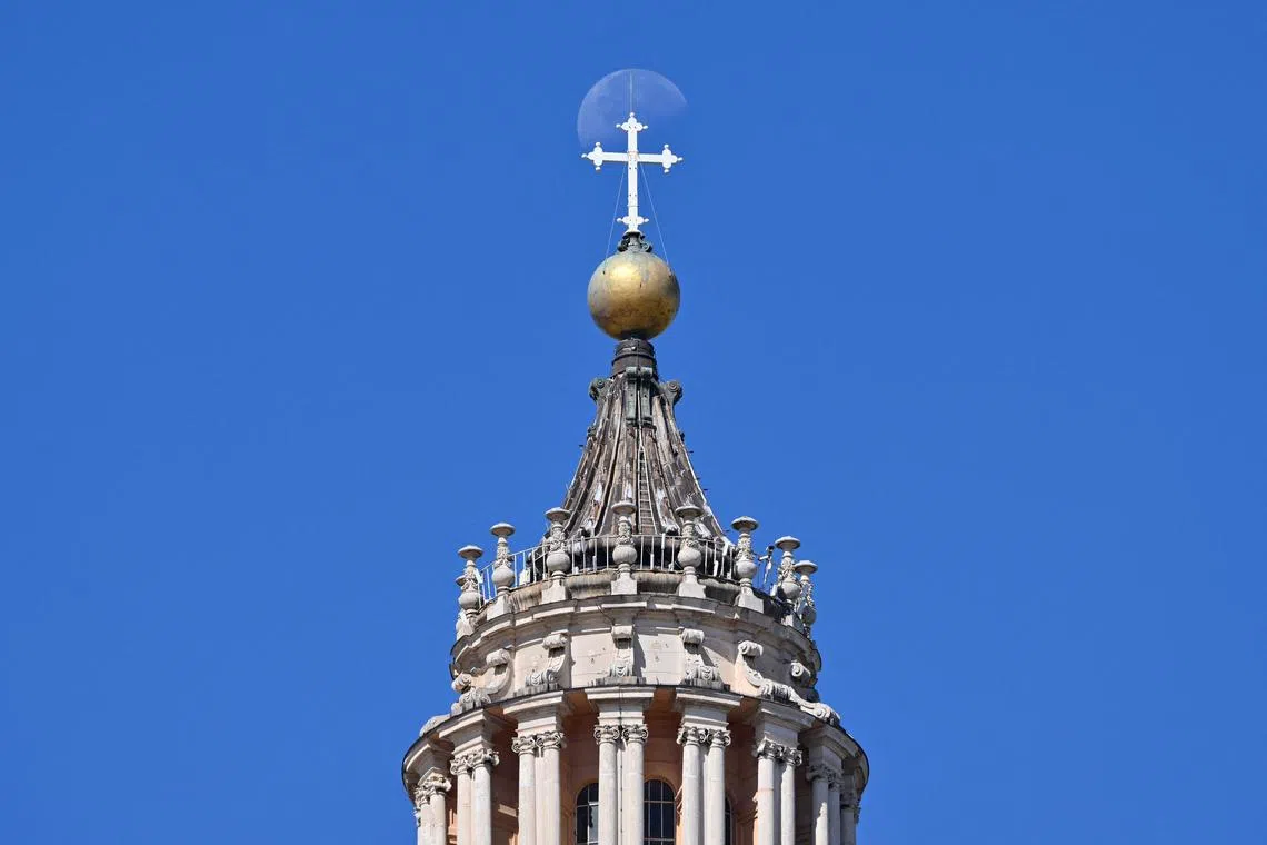 A full moon rising behind the cross atop the dome of St. Peter's Basilica in St. Peter's Square at the Vatican on August 25, 2024.