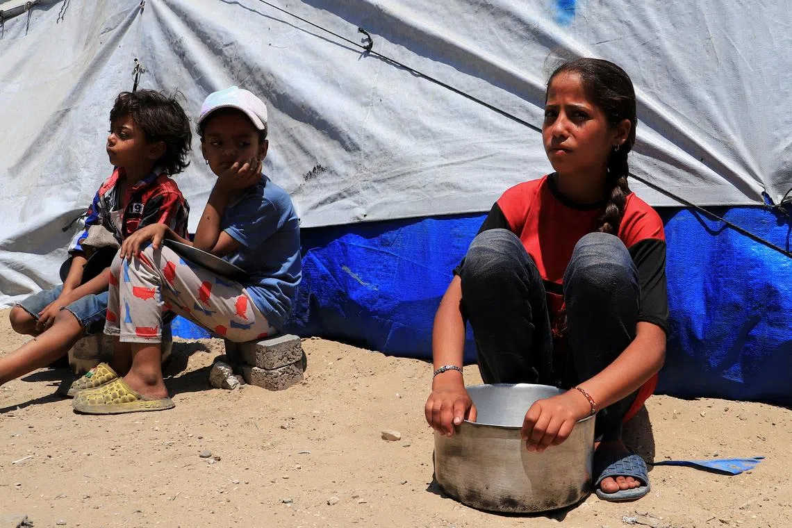 FILE PHOTO: Displaced Palestinian children, one with an empty pot, sit while waiting to receive food from a charity kitchen, in Gaza City, June 3, 2025. REUTERS/Ebrahim Hajjaj/File Photo