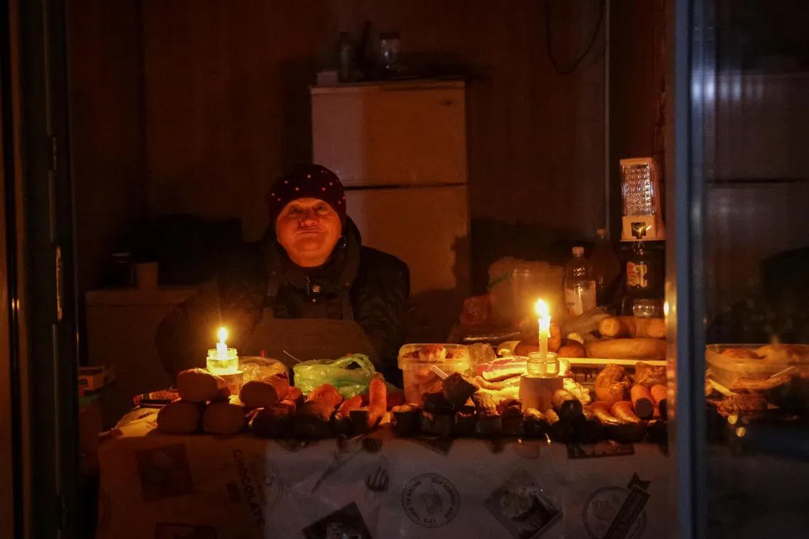 A vendor in Odessa waits for customers in a small store that is lit with candles after critical civil infrastructure was hit by Russian missile attacks.