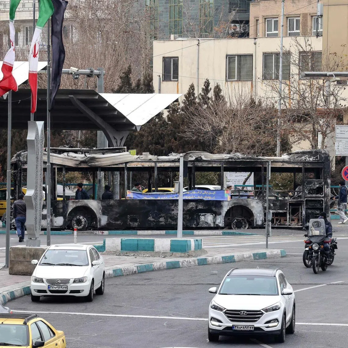 Traffic driving past the wreckage of a burnt-out bus in Tehran's Sadeghieh Square on Jan 15.