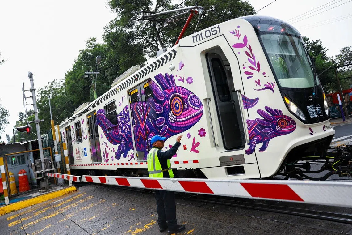A crossing keeper gestures as a train car featuring an image of the critically endangered axolotl, a salamander native to central Mexico's lakes, passes by, in Mexico City, Mexico, May 27, 2026. The use of axolotl in public imagery ahead of the FIFA World Cup 2026 has divided residents who say more should be done to protect its habitat. REUTERS/Raquel Cunha     TPX IMAGES OF THE DAY