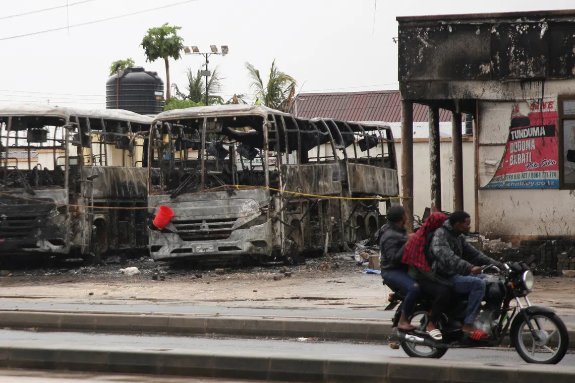 People ride a motorcycle past the wreckage of buses burnt during protests, following a general election marred by violent demonstrations over the exclusion of two leading opposition candidates, at the Mwembechai area in Kinondoni district in Dar es Salaam, Tanzania, November 4, 2025. REUTERS/Emmanuel Herman