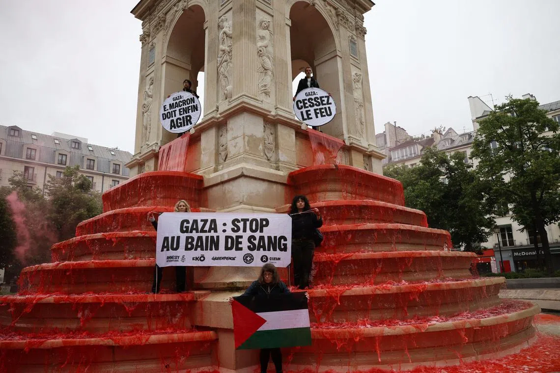 Activists hold a Palestinian flag and placards after pouring red paint into the Fountain des Innocents in Paris..