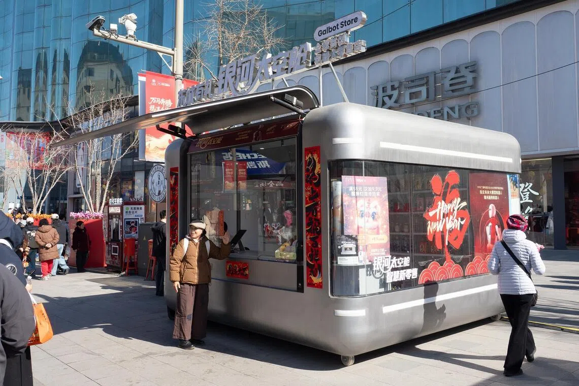A passer-by poses for a photo with the Galbot robot self-service shop at Wangfujing shopping street in Beijing.