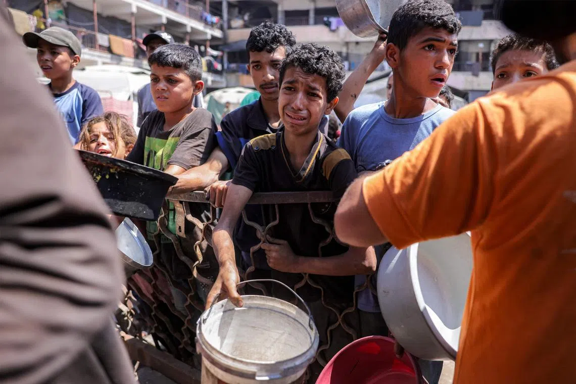 Children queue with pots to receive meals from a charity kitchen in Gaza City on July 14.