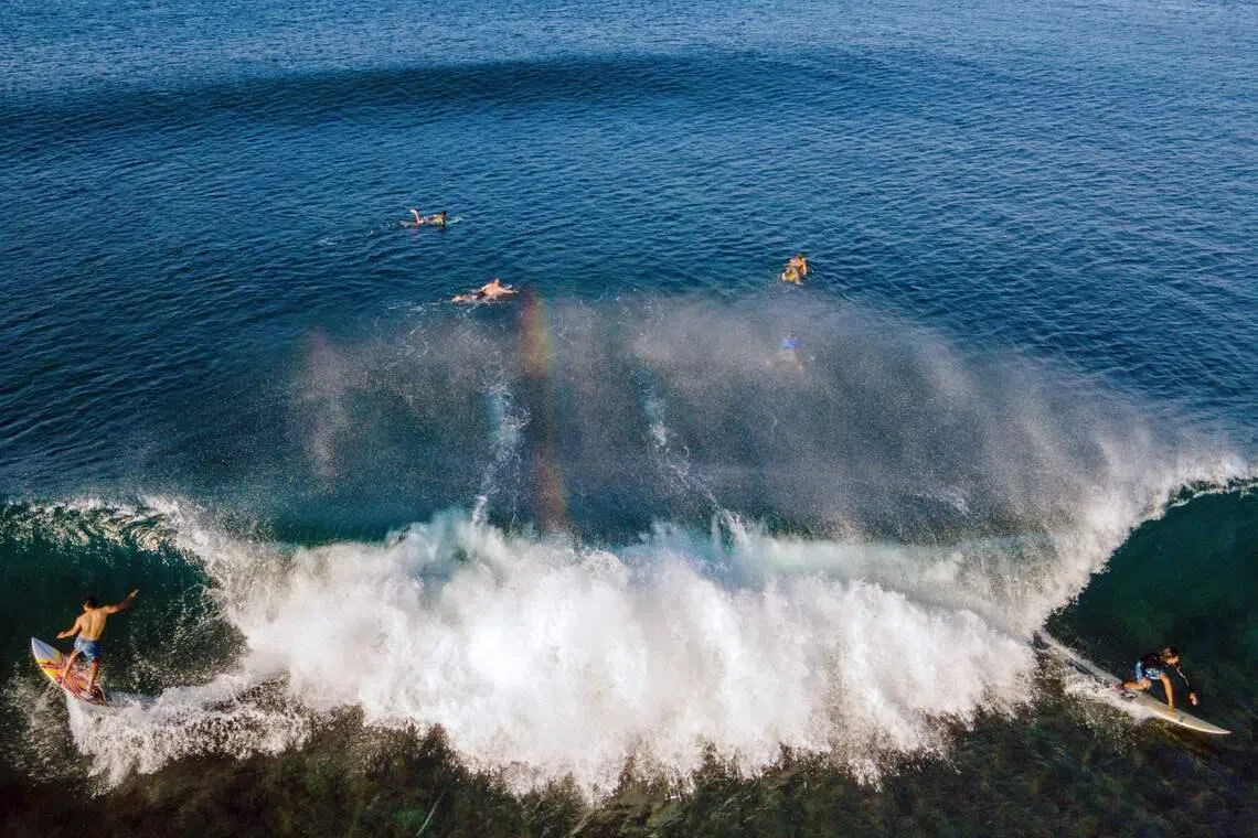 Surfers riding a wave in Lhoknga beach, Indonesia's Aceh province, on Jan 12, 2026. 