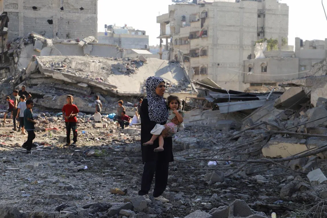 A Palestinian woman carries a child, as they inspect the site of an overnight Israeli strike on a house, in Gaza City, on Aug 26, 2025.